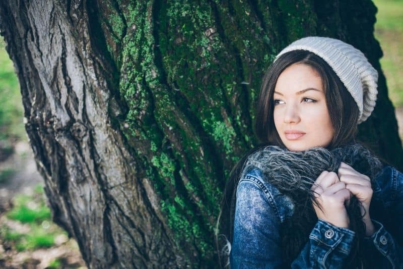 donna pensierosa che si nasconde dietro il grande albero con giacca e cuffia