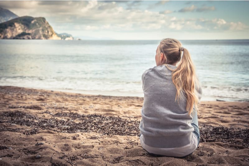 pensive woman sits near the sea looking far