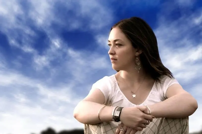 pensive woman sitting with blue sky as her background