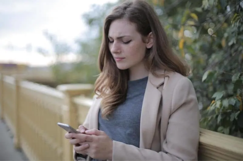 pensive woman using smartphone outdoors leaning on the railings wearing coat