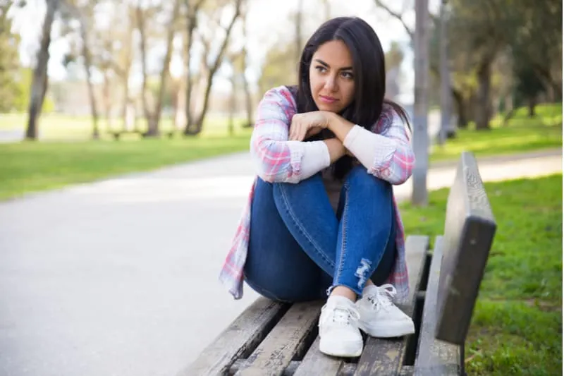 pensive young woman sitting with feet on the bench in the park