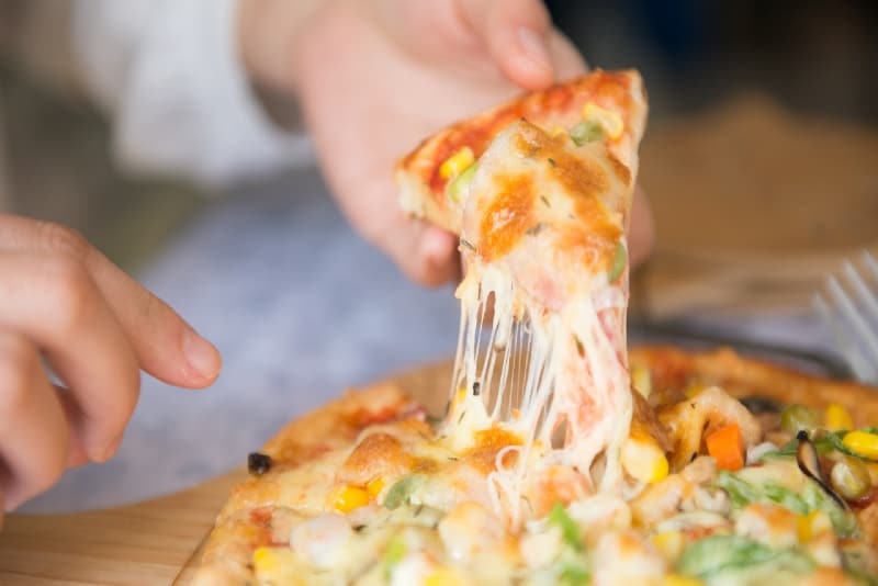 person holding a slice of pizza with cheese