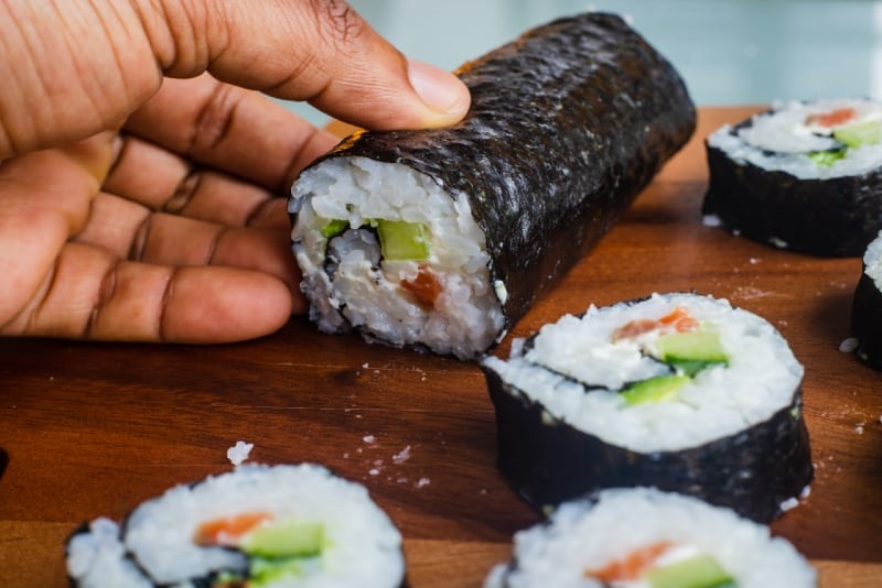 persona che tiene in mano un rotolo di sushi su un tavolo di legno marrone