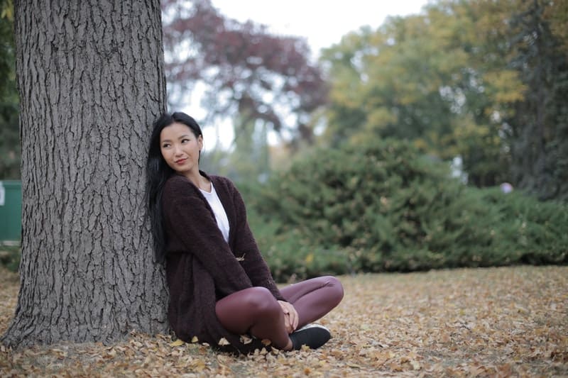 senhora asiática positiva sentada debaixo de uma árvore