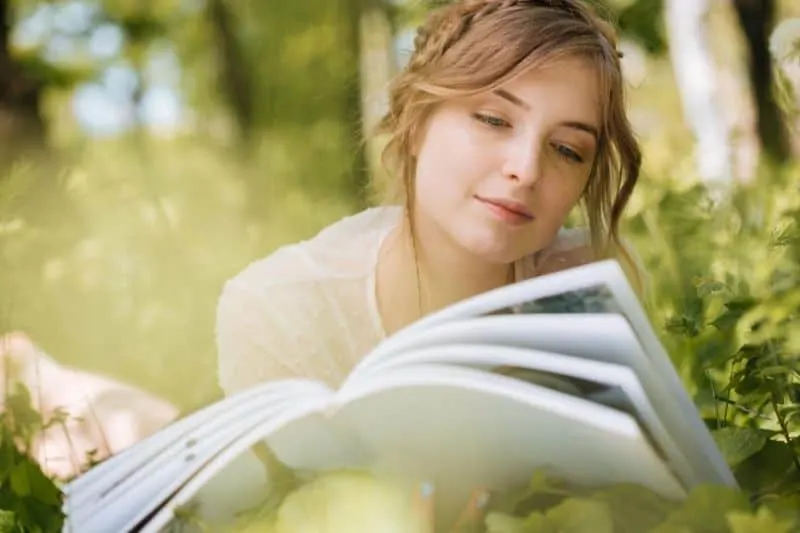 pretty and pensive woman reading magazine outdoors while lying down