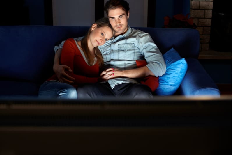 romantic movie night between couples hugging tight while sitting in the couch at home