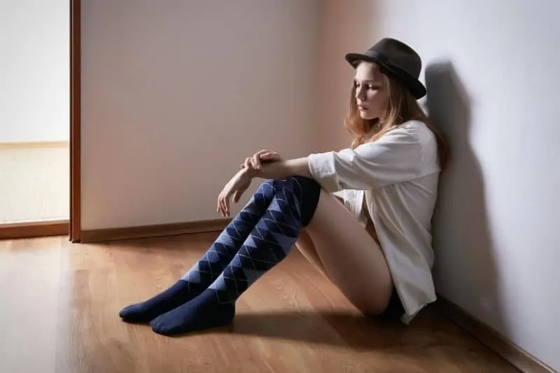 sad pensive woman sitting on the floor inside a room wearing hat and a knee sock