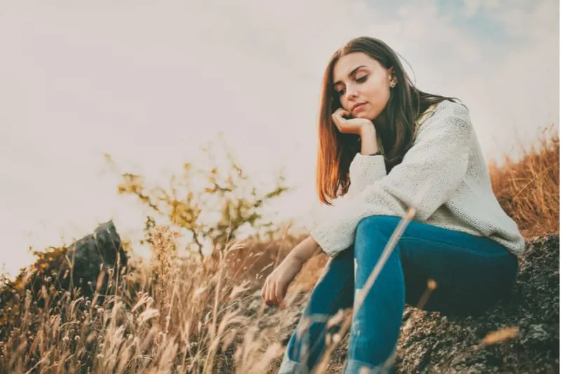 sad young lady sitting in the meadow deeply thinking