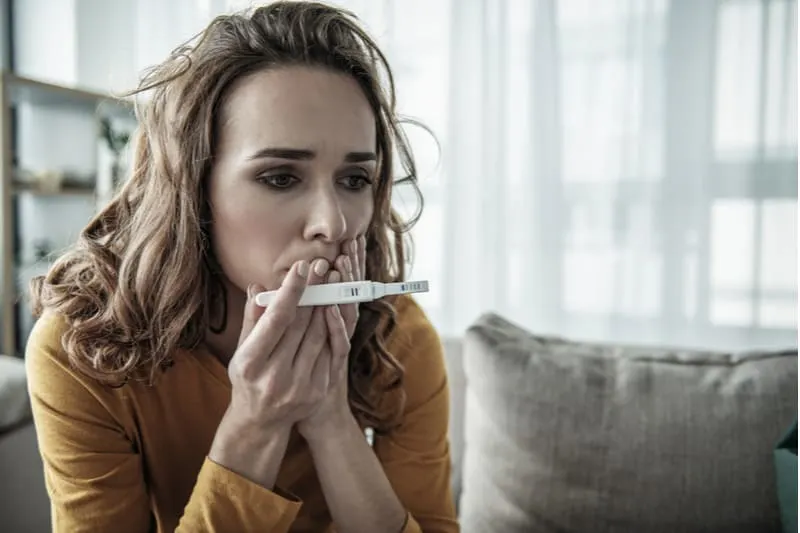 scared woman sitting holding a pregnancy test