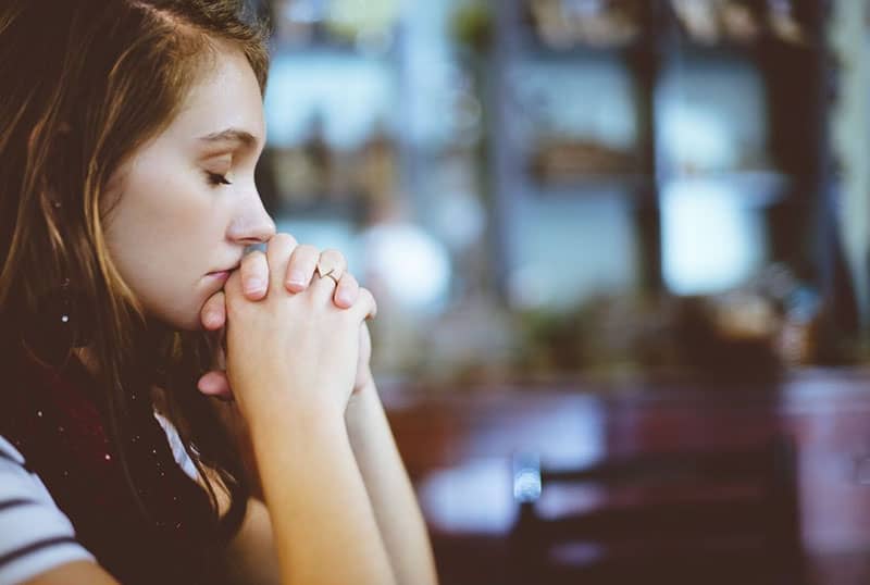 vista lateral de una mujer rezando dentro de un establecimiento difuminado