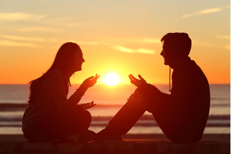 silueta de una pareja conversando junto al rompeolas cerca del mar durante la puesta/salida del sol