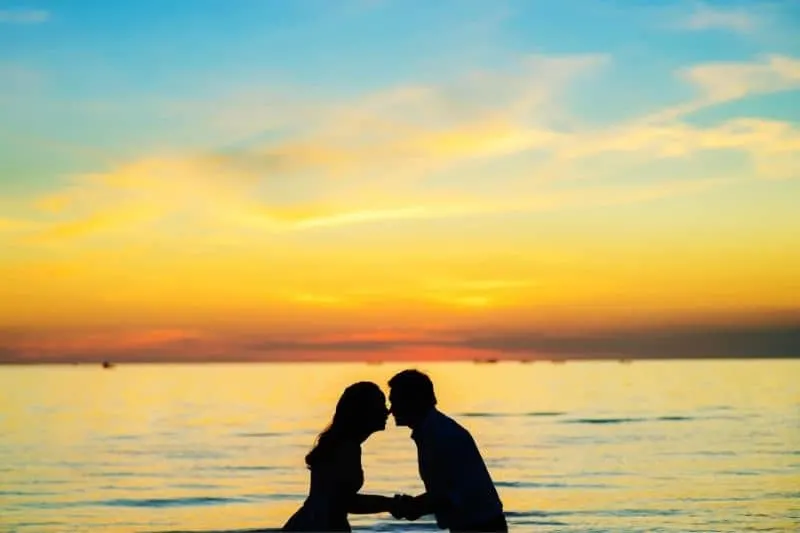 silhouette of a couple nose to nose and holding hands by the beach during sunset