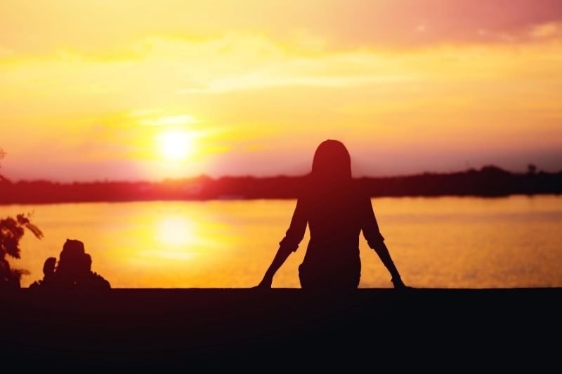 silueta de mujer sentada en una hermosa puesta de sol a orillas del río