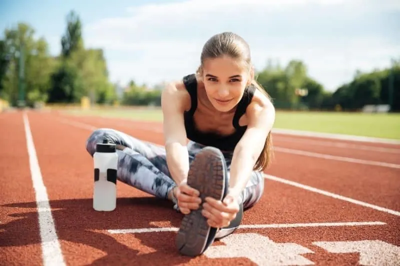 smiling woman athlete stretching in the middle of the tracking field