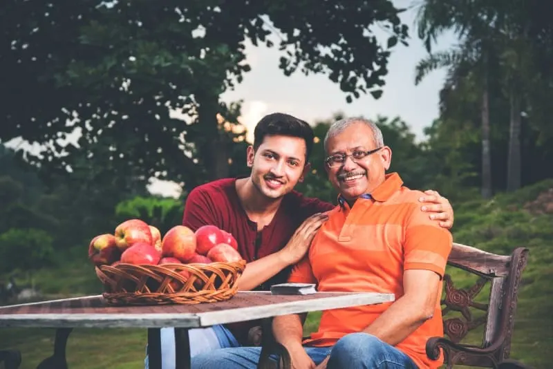 indian son hugging father while sitting at table