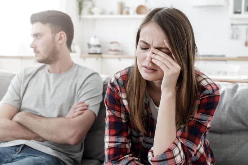 mujer estresada llorando sentada junto a un hombre alterado