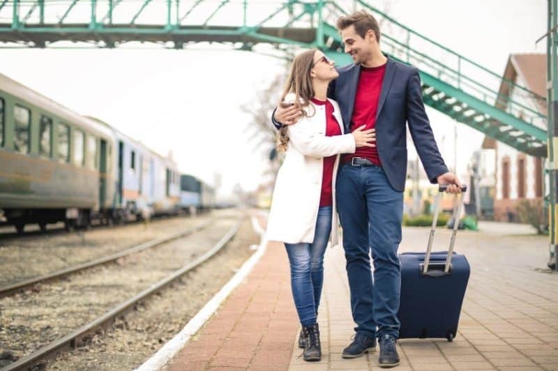 dolce coppia che cammina con i bagagli lungo le rotaie del treno