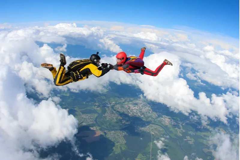 two people skydiving holding hands in air with clouds beneath them