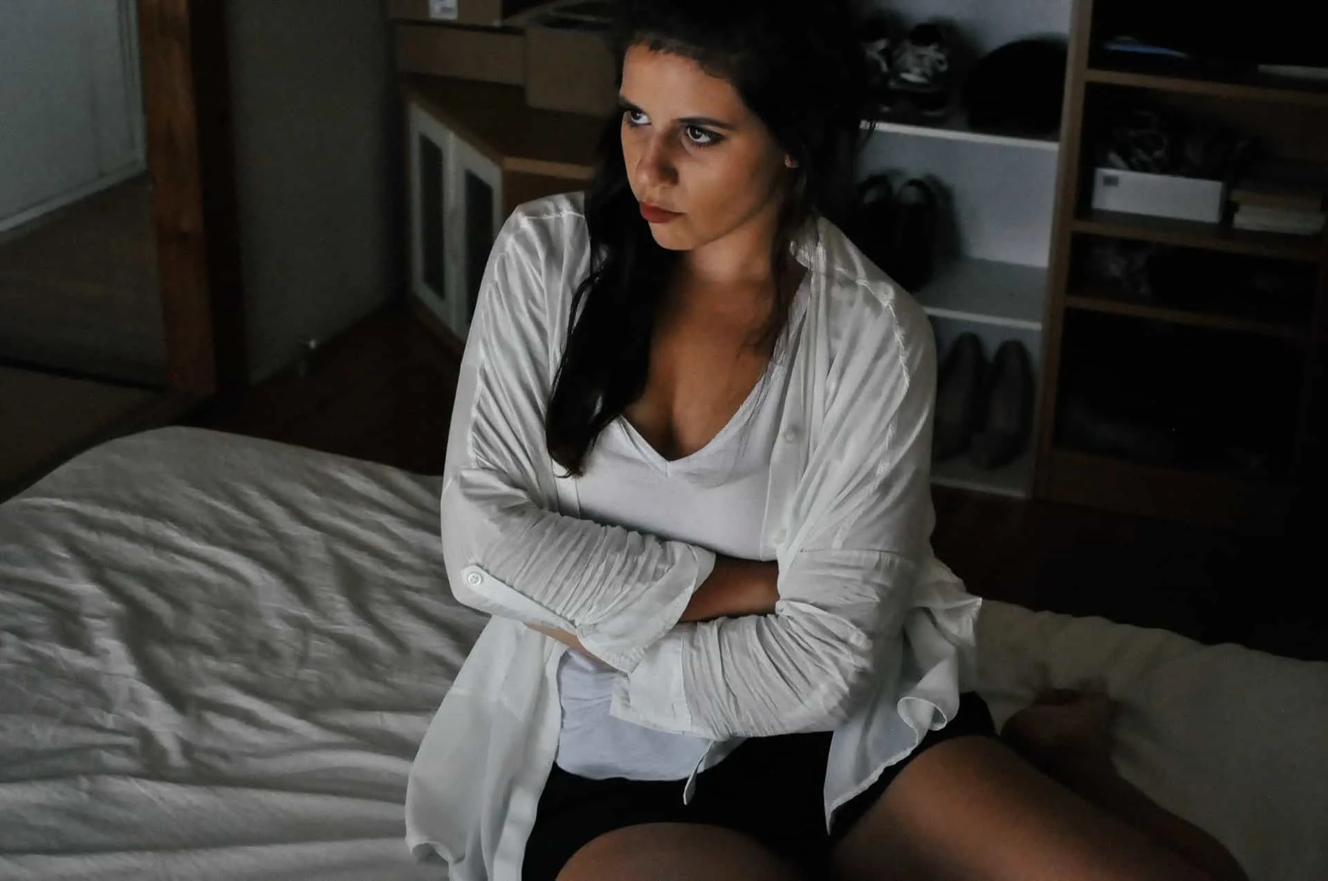 upset woman sitting on bed wearing white top