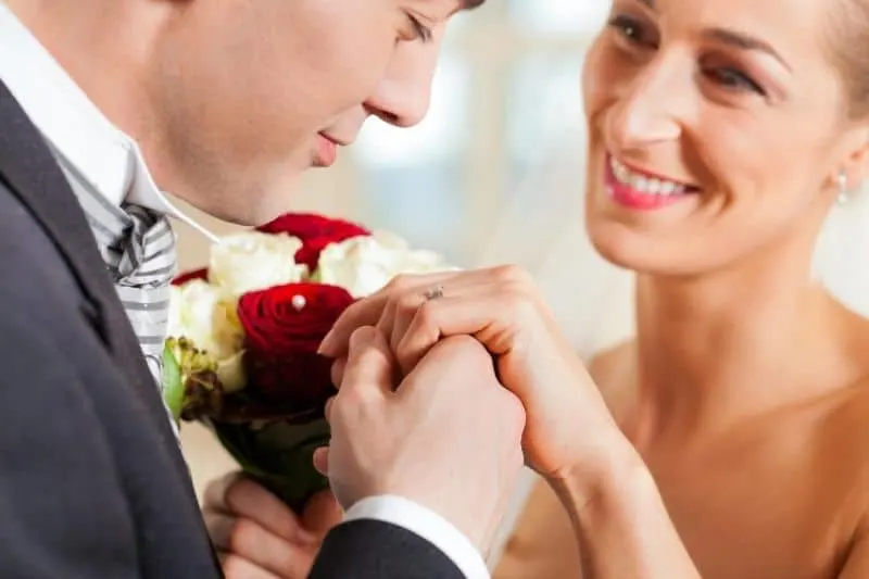 wedding couple promising man holding hand of the woman carrying buoquet of flowers