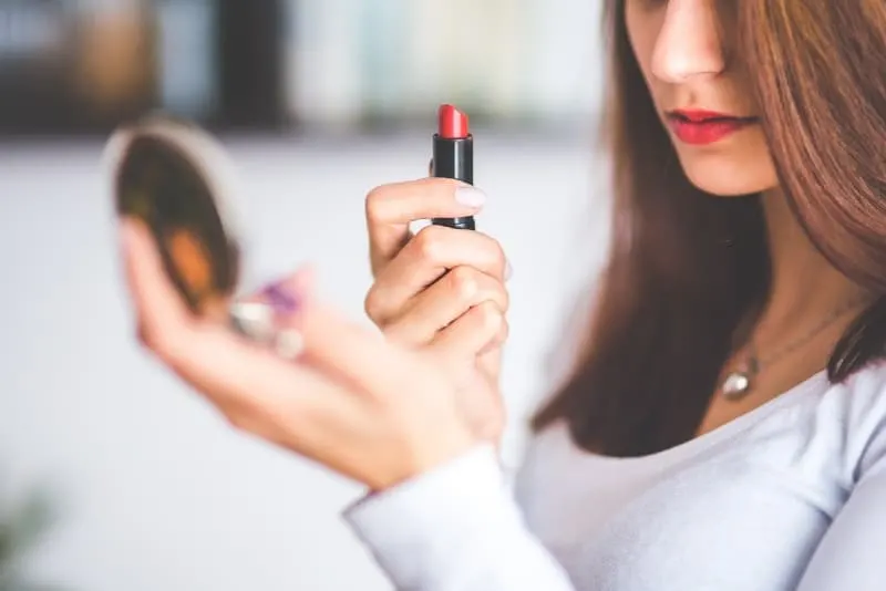 woman doing lipstick while holding little mirror