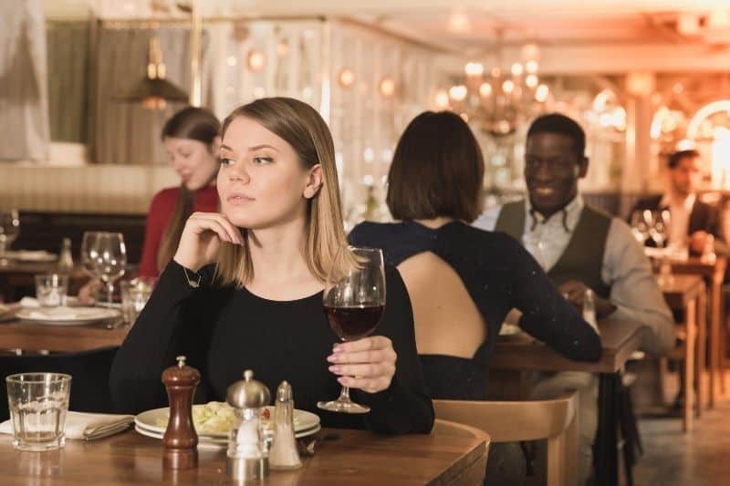 donna che mangia al ristorante con in mano un bicchiere di vino pensando