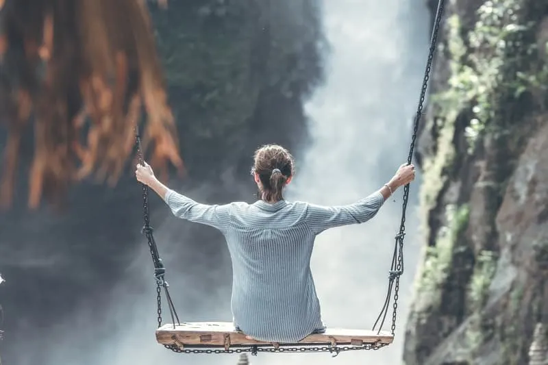 woman facing a waterfall while swinging on a big swing