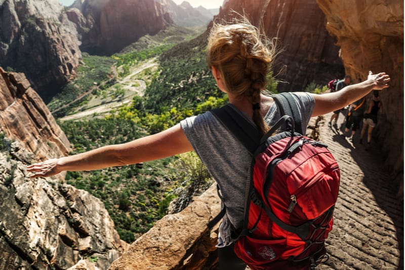 mujer excursionista de pie en la ladera de la montaña con los brazos en alto 