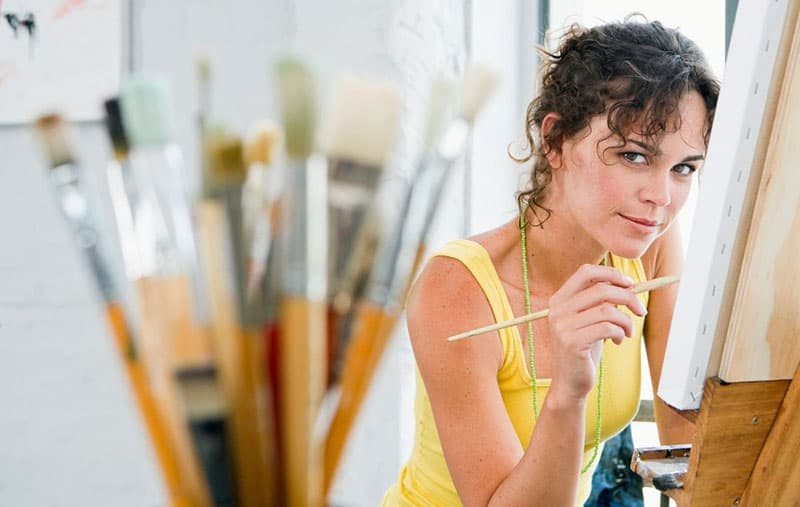 donna che tiene un pennello da pittura di fronte a una tela