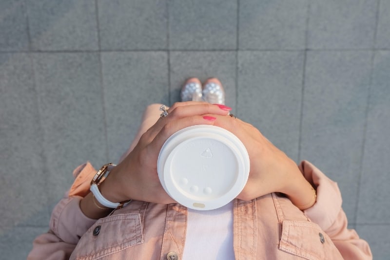 donna che tiene una tazza bianca usa e getta in piedi all'aperto