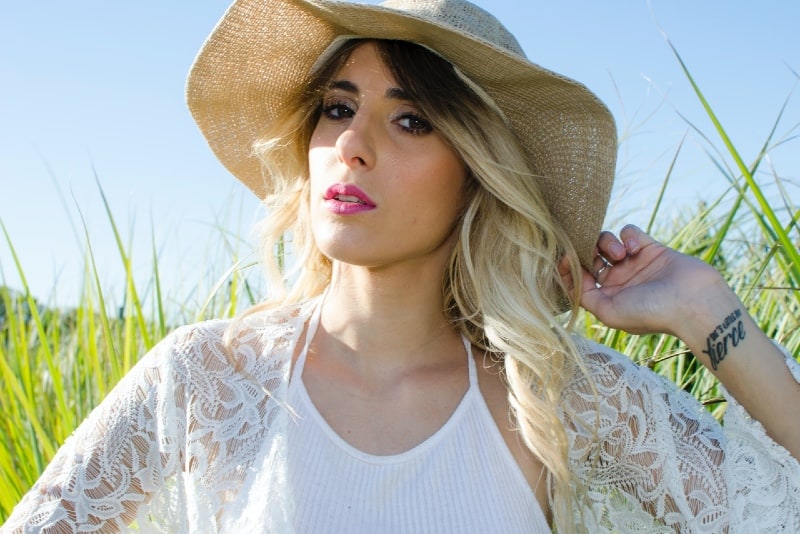 woman holding hat while standing on grass field