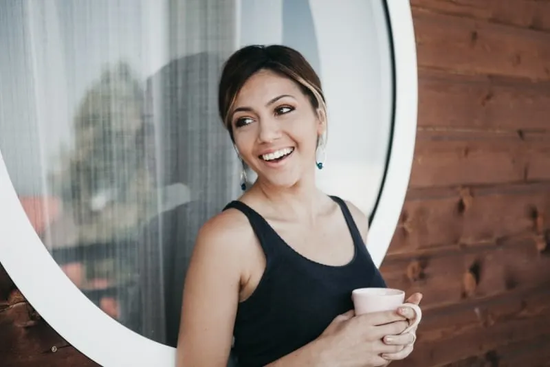 woman holding mug while standing near window