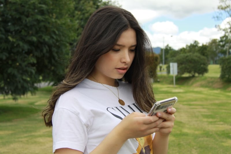 Mulher com t-shirt branca estampada a segurar o telemóvel ao ar livre