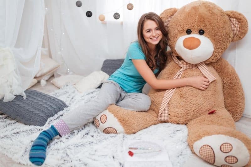 woman hugging lifesize teddy bear lying on bed inside bedroom
