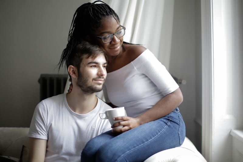 woman with mug hugging man while sitting on sofa