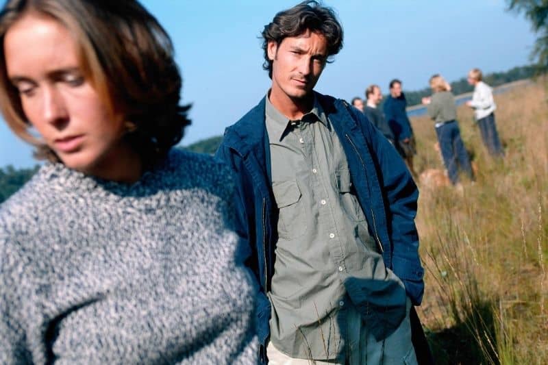 woman ignoring man on focus standingin the grassfield with people on background