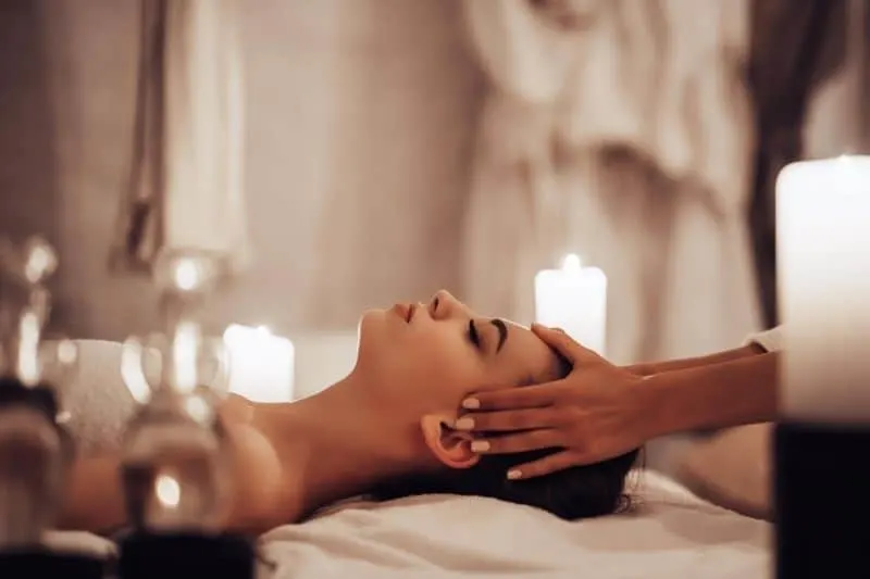 woman in a spa salon being massaged at her head by a therapist surrounded with candles