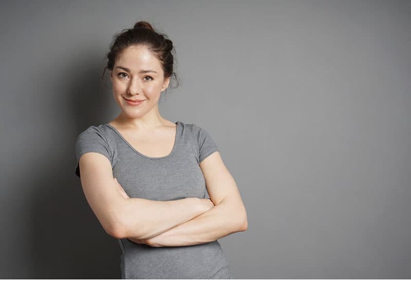 woman in messy bun wearing gray top standing against gray wall