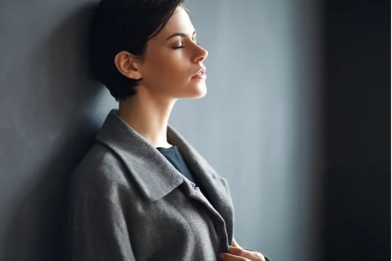 woman leaning on gray wall closing her eyes and wearing office wear