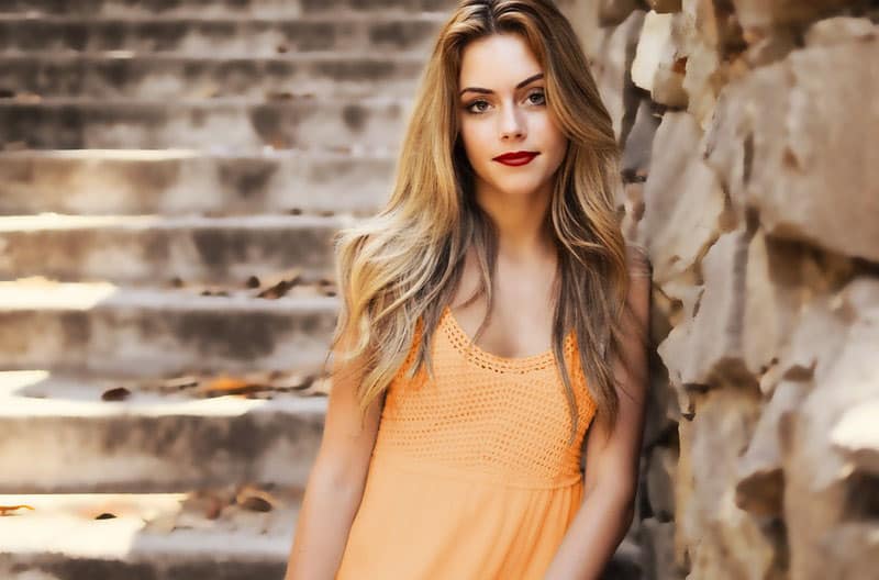 woman leaning on rock wall wearing orange tank top with stairs behind her