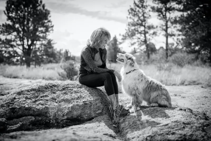 smiling woman looking at dog while sitting on rock