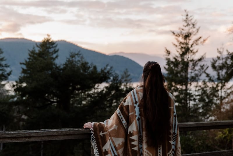 long haired woman in printed poncho looking at mountain