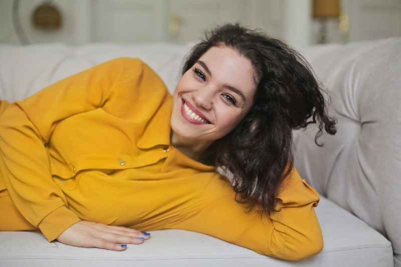 donna sorridente in camicia gialla sdraiata sul divano