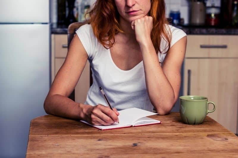 woman making notes sitting by a small table drinking coffee