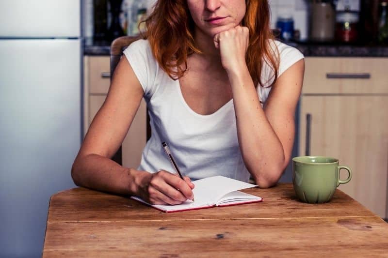 mujer tomando notas sentada junto a una mesita bebiendo café