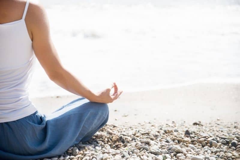 mujer meditando en la playa en posicion de loto mostrando solo el lado derecho del cuerpo