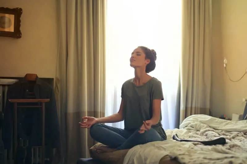 woman meditating in bed inside bedroom with semi open curtains