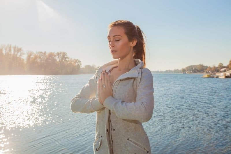 mujer meditando al aire libre de pie cerca de la masa de agua