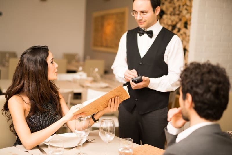 mulher a pedir uma refeição ao empregado de mesa enquanto está sentada perto de um homem