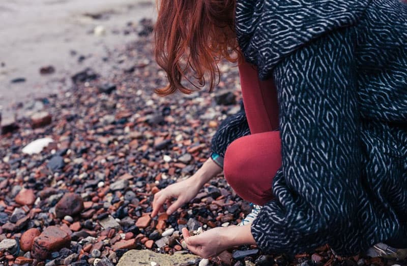 mujer recogiendo piedras cerca de una masa de agua